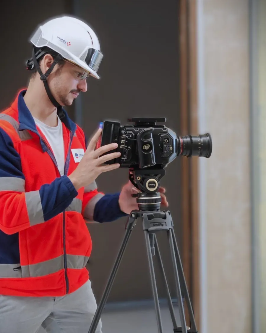 Axel Milon filming on a construction site: hard hat, high-visibility vest, camera on a tripod